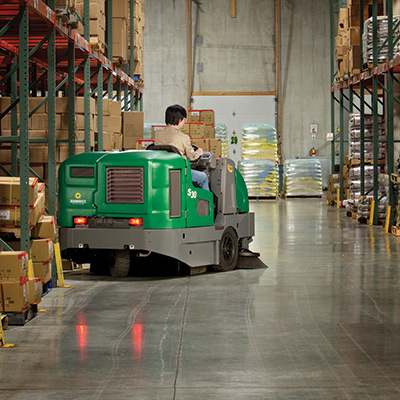 Someone riding a sweeper inside of a warehouse building.