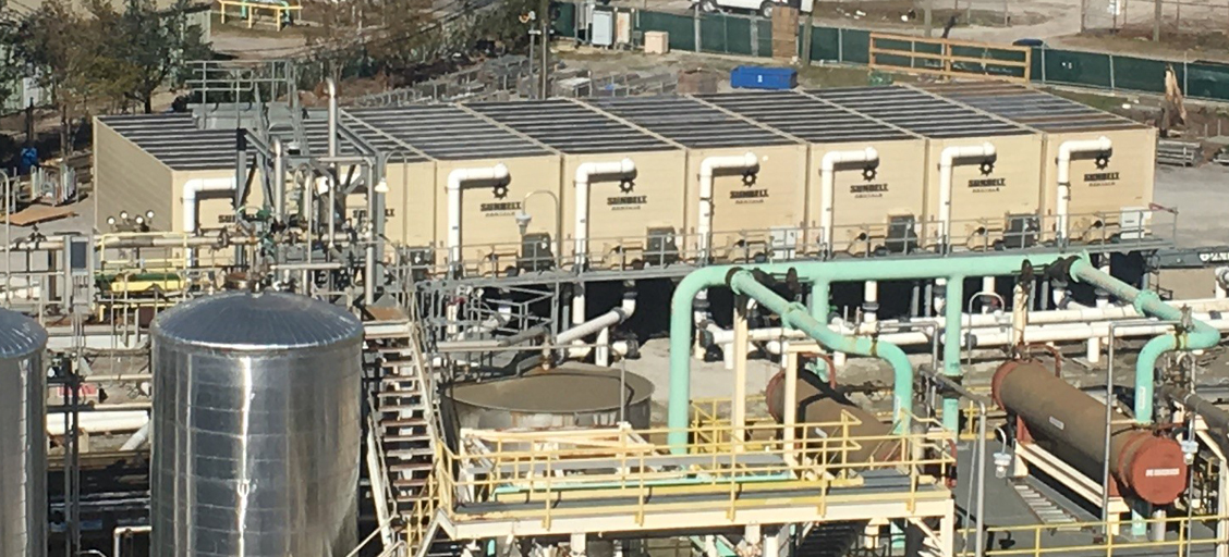 An aerial view of eight Sunbelt Rentals cooling towers connected to an industrial plant facility, identified by large industrial pipes connected to holding tanks, a number of catwalks and viewing platforms.